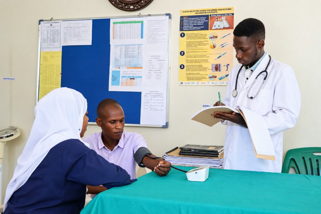 A KICoB clinician consults a student while another staff member records the visit at the campus dispensary.